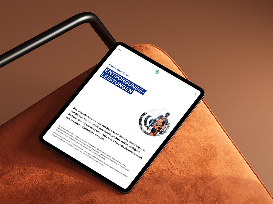 Tablet mit geöffneter Website der Hans Hirzinger GmbH, positioniert auf einer braunen Sitzfläche. Der Bildschirm zeigt die Rubrik 'Entsorgungsleistungen' mit einem klaren Layout für eine einfache Navigation.
