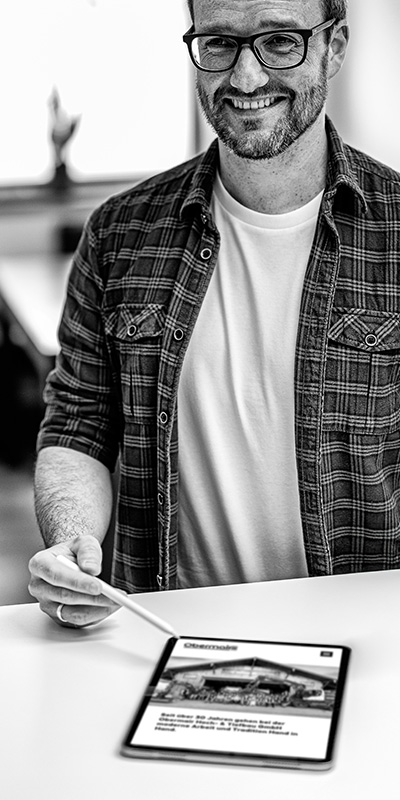 Florian Bechtler hält einen digitalen Stift und zeigt auf ein Tablet, das einen klickbaren Webdesign-Prototyp anzeigt. Die interaktive Vorschau ermöglicht das Testen der Benutzerführung.