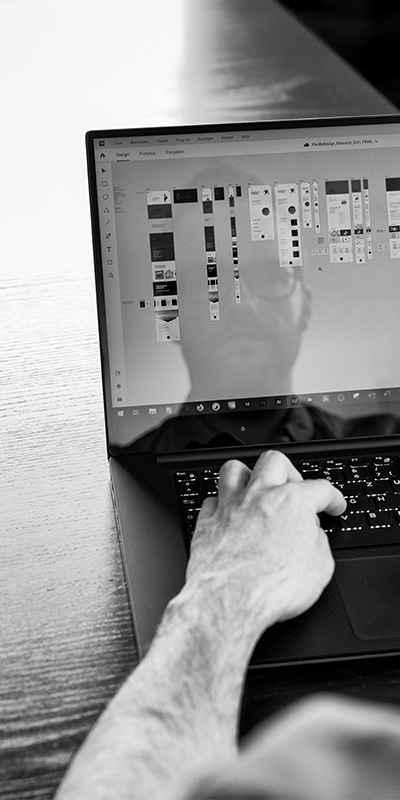 Nahaufnahme eines Laptops mit geöffneter Webdesign-Software. Eine Hand navigiert durch verschiedene UI-Elemente und Layouts, um das Design auf Benutzerfreundlichkeit und Performance zu testen.